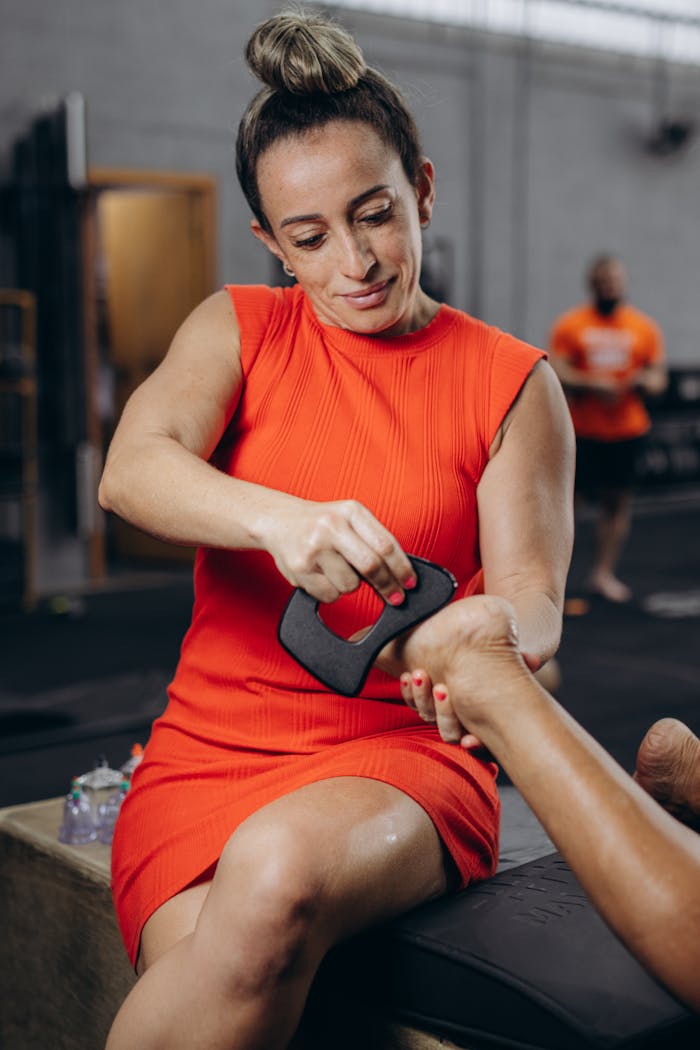 Woman in a red dress performing a hand massage with a tool at a gym setting, promoting wellness.