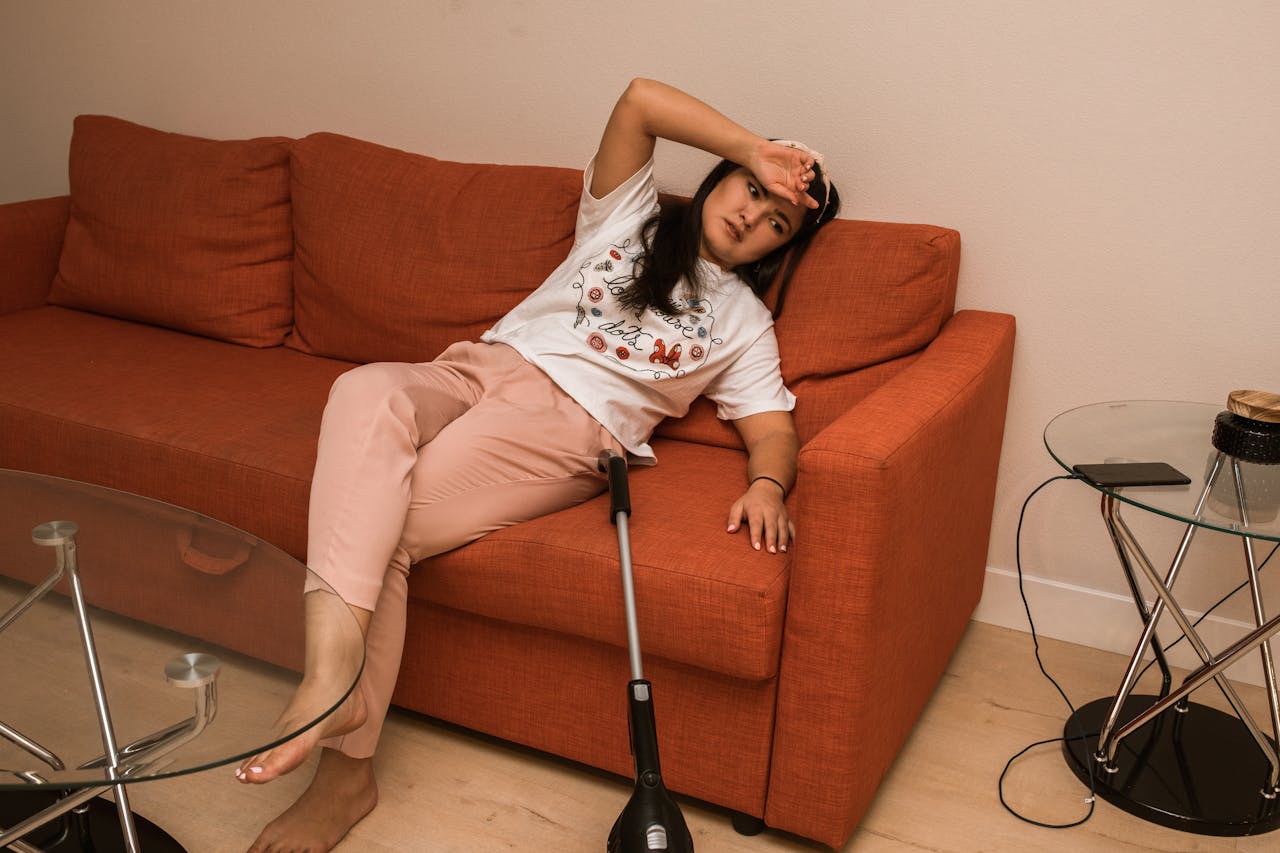 about-us Asian woman resting on orange sofa with crutch, indoors, casual attire.